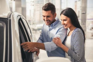 Visiting car dealership. Beautiful couple is examining a new car and smiling