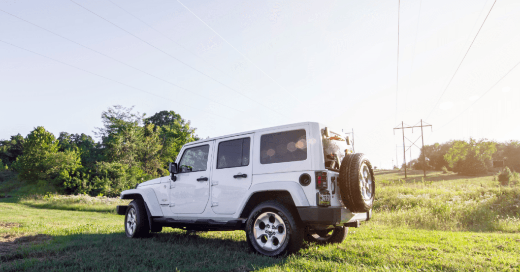 white jeep in a green field with power lines in the background