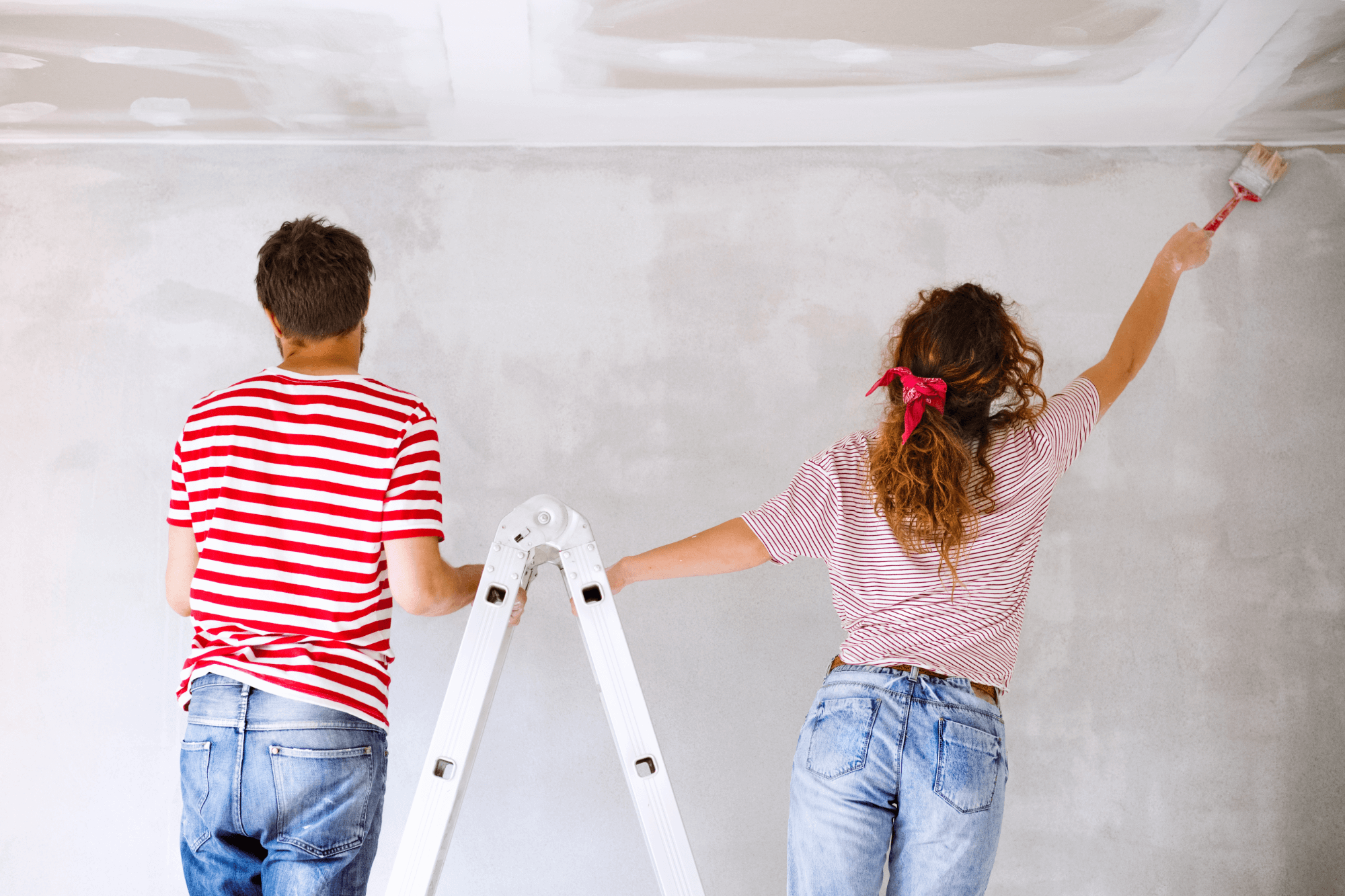 Man and woman standing on ladder painting walls of room