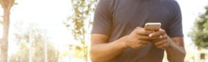Man looking at cell phone outside with trees behind him