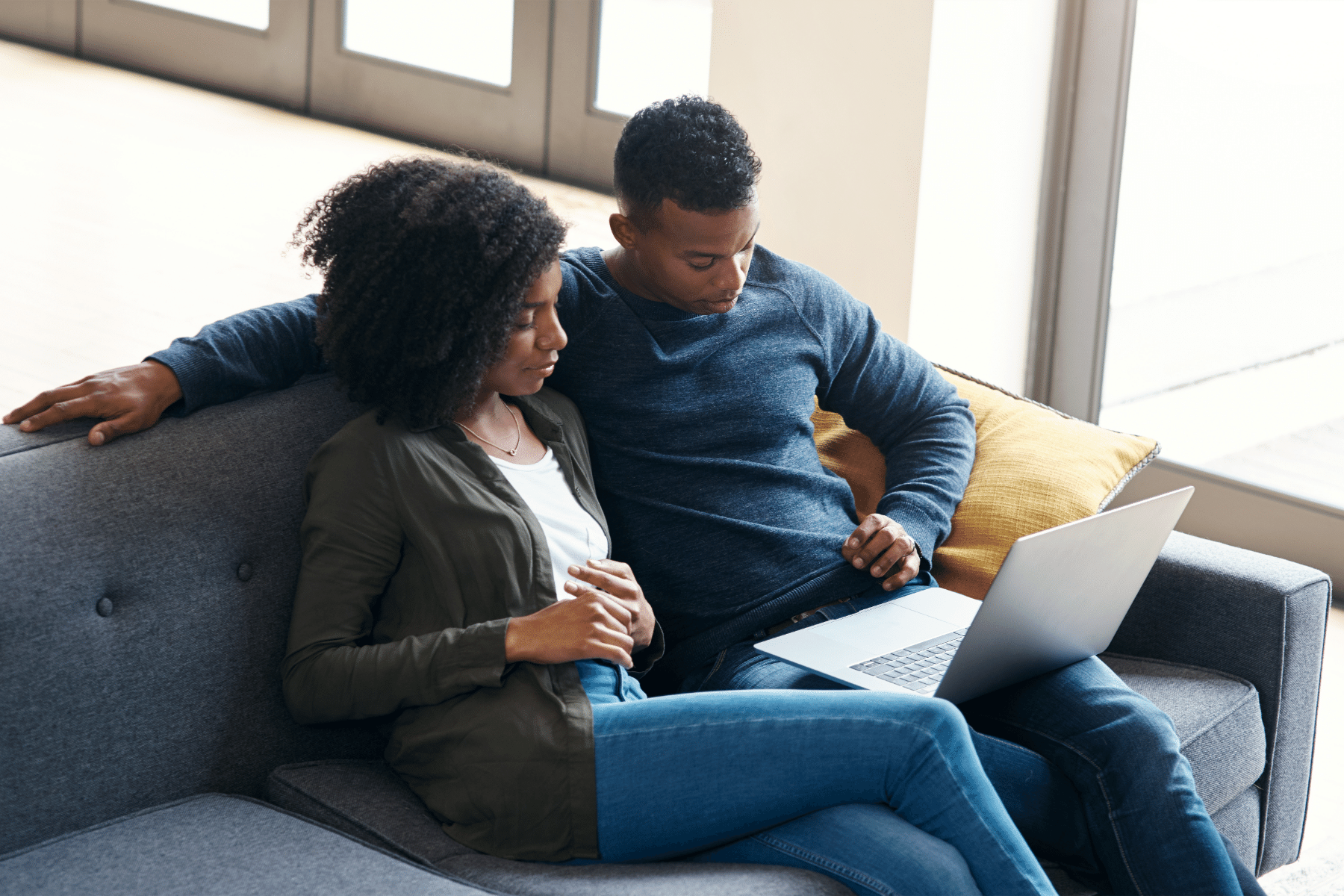 Young couple sitting next to each other on couch looking at laptop