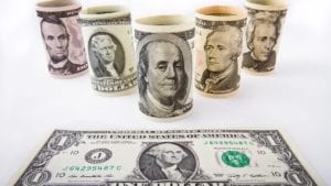 $5, $10, $20, $50 and $100 bills rolled up sitting on surface with $1 bill laying flat in front of them