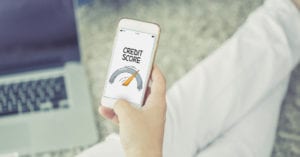 Person sitting on carpet with laptop in front of them and holding phone with credit score on screen